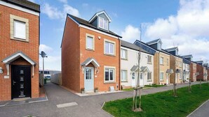 Une rangée de maisons de ville modernes aux façades en briques, aux toits à deux versants et aux petits jardins avant.