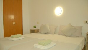 Habitación de hotel con dos camas, un armario de madera, una mesita de noche con lámpara y una luz de pared.