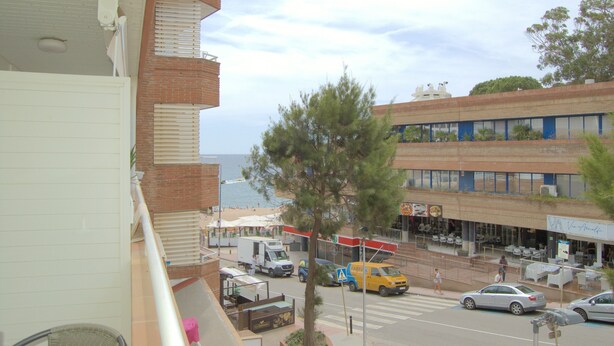 Vista de la calle con un edificio que tiene un balcón, un árbol y vista a la playa.