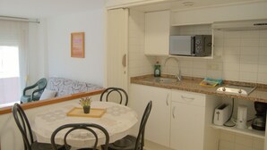Cocina compacta con microondas, lavamanos y electrodomésticos básicos. Hay una zona de comedor con mesa y sillas.