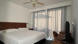 Une chambre d’hôtel avec un grand lit, un bureau avec un ordinateur et un ventilateur de plafond.