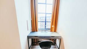 Een kleine, moderne kamer met een bureau, stoel en een raam met gordijnen.