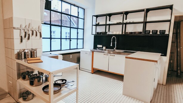 Een moderne keuken met witte kasten, een zwarte achterwand en een raam dat natuurlijk licht binnenlaat.