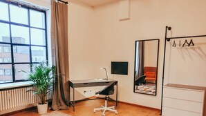 Een moderne slaapkamer met een bed, een bureau, een stoel, een radiator, een kamerplant en een raam met gordijnen.