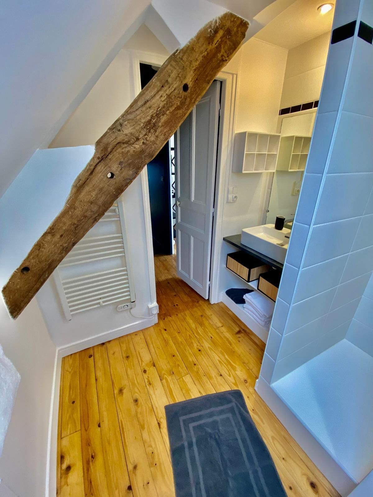 A modern bathroom with a wooden beam ceiling, a white sink, and a tiled shower area.