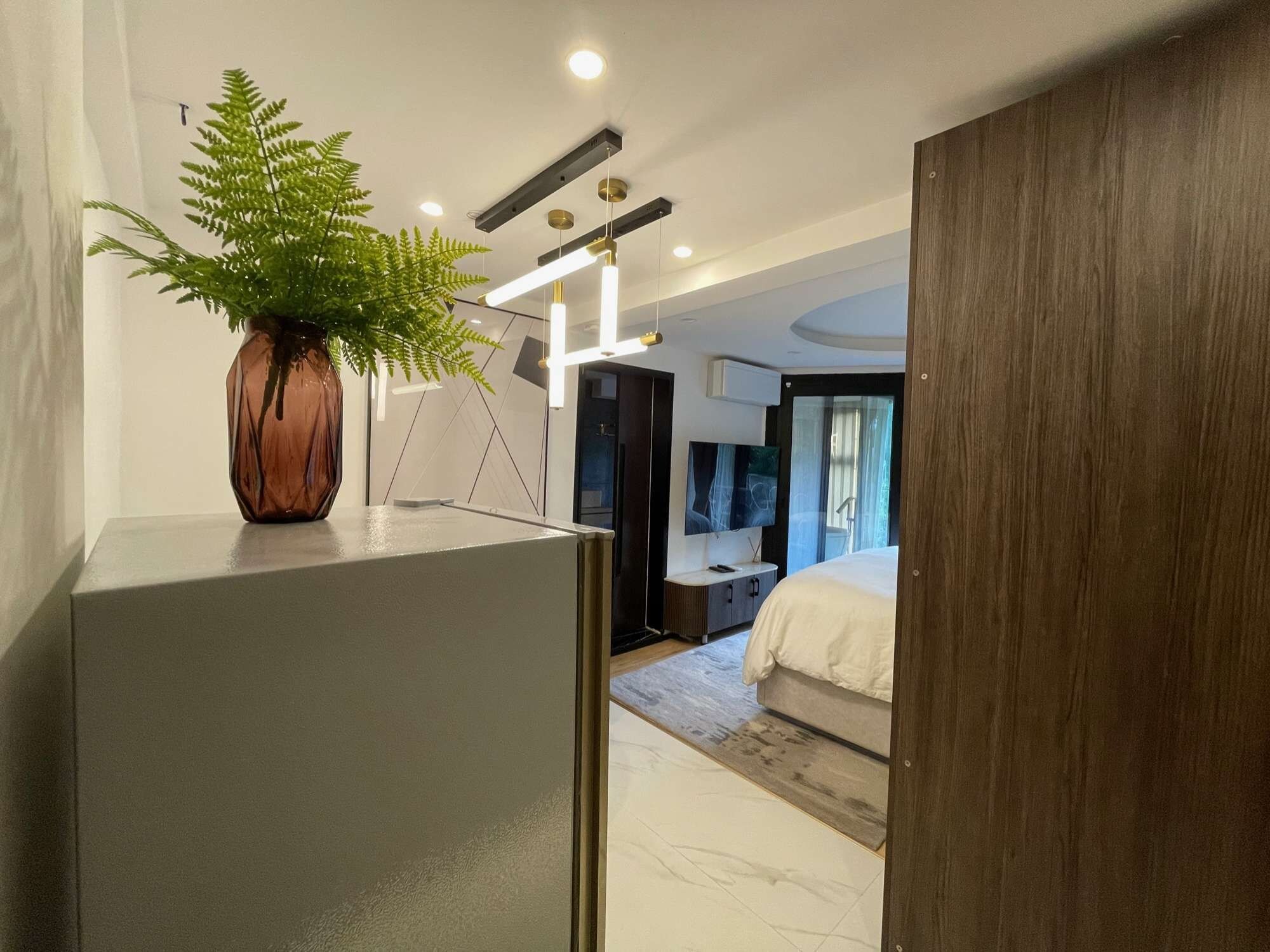 A modern bedroom with a large bed, a TV, and a plant in a vase.