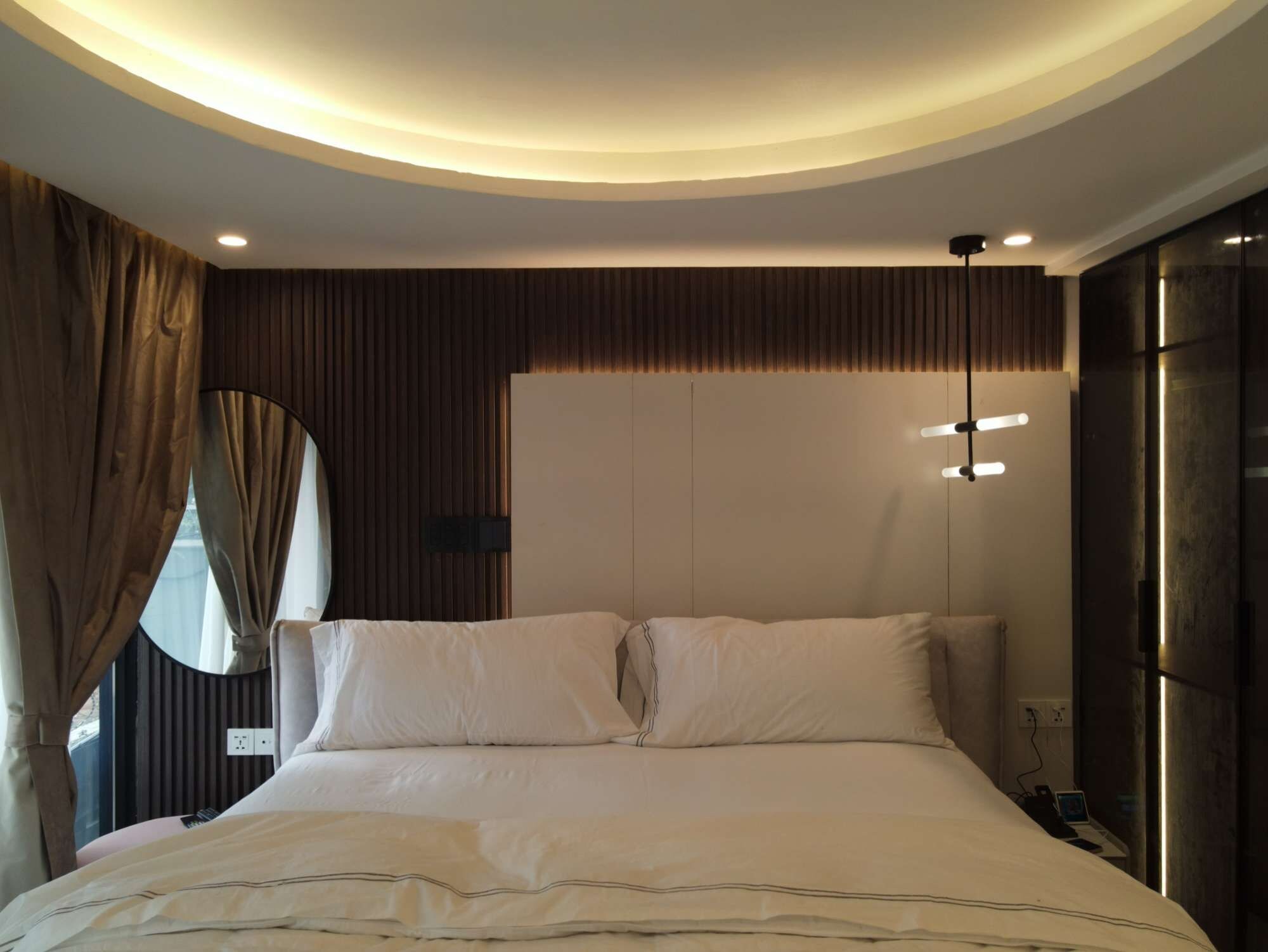 Une chambre moderne avec un grand lit, un miroir rond et un luminaire fixé au plafond.