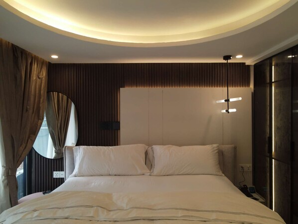 Une chambre moderne avec un grand lit, un miroir rond et un luminaire fixé au plafond.