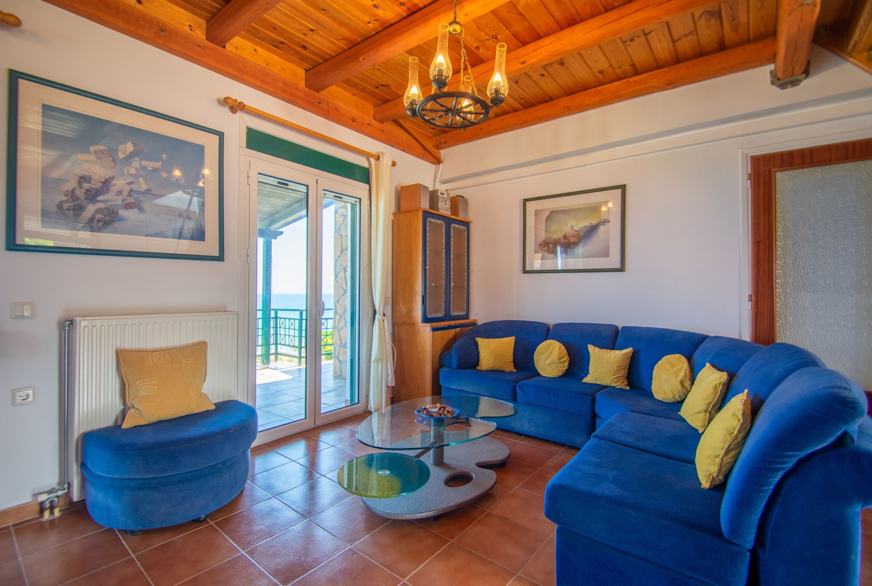 A living room with a blue sofa, a glass coffee table, and a wooden ceiling.