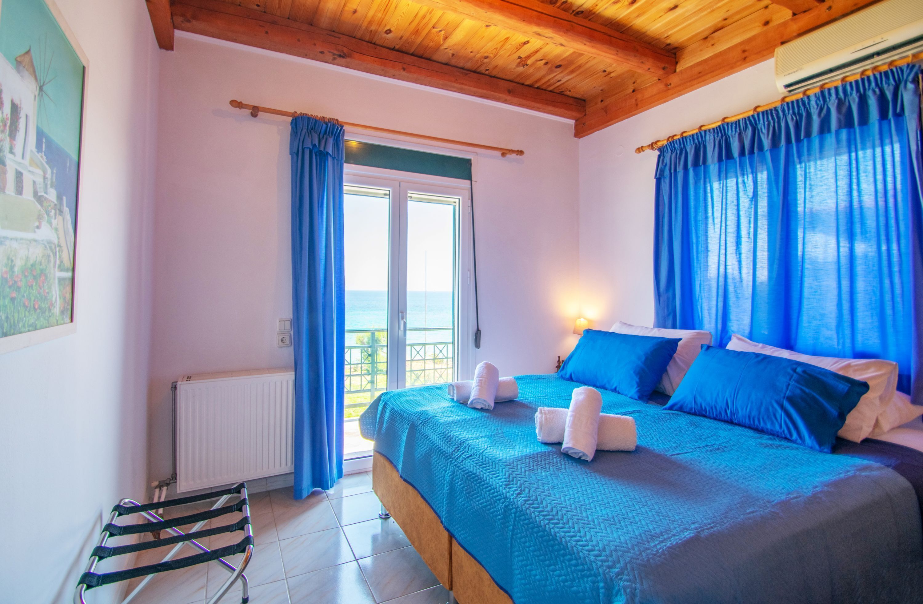 Un dormitorio con cama, cortinas azules, vista al mar y techo de madera.