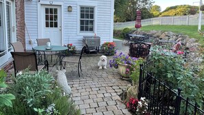 Eine Terrasse mit Gartenmöbeln, einem Hund und einem Garten mit Blumen und einem Zaun.