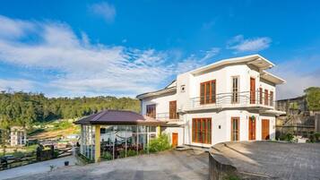 Ein weißes, zweistöckiges Gebäude mit Balkon, umgeben von Pflaster und Grünflächen.