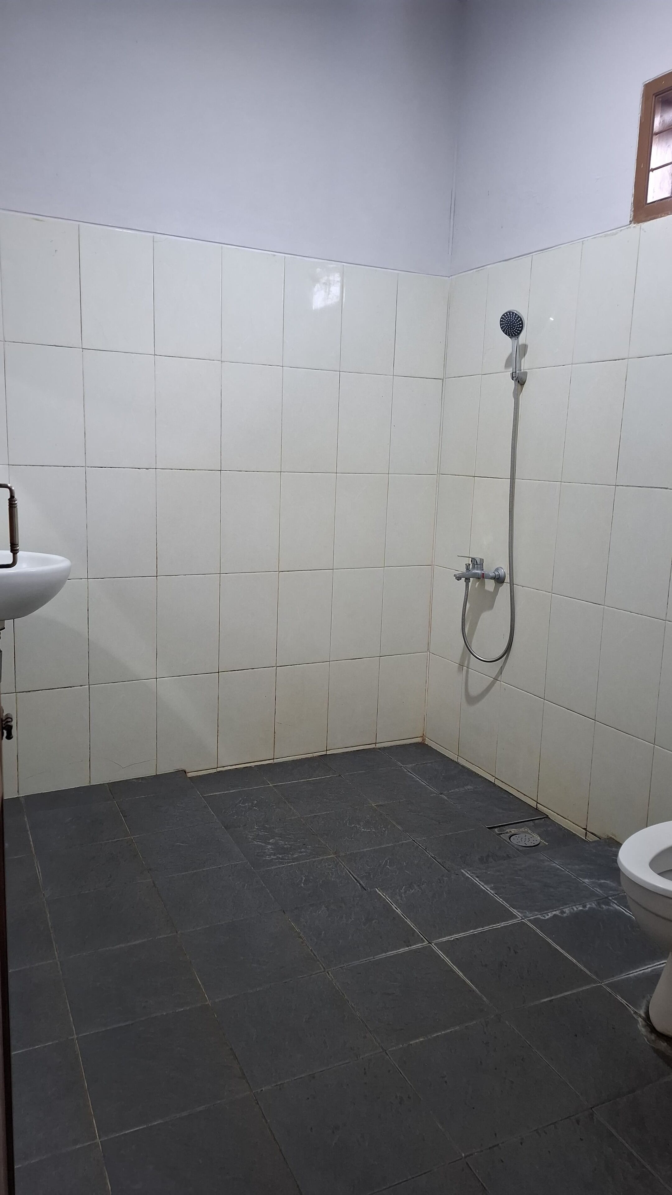 Ein Badezimmer mit weißen Fliesen, dunklem Boden, einem Waschbecken, einer Dusche und einer Toilette.