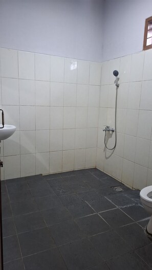 Ein Badezimmer mit weißen Fliesen, dunklem Boden, einem Waschbecken, einer Dusche und einer Toilette.