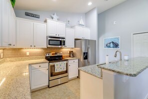 Una cocina con armarios blancos, un refrigerador de acero inoxidable, un microondas y una estufa.
