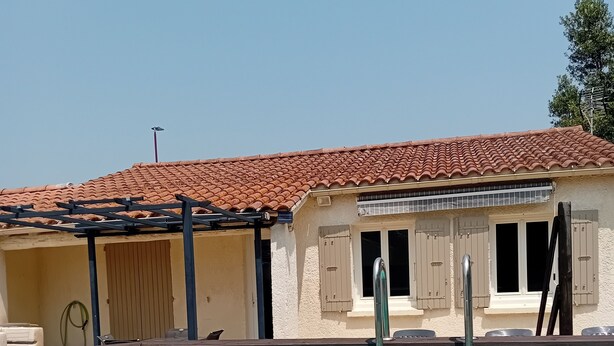 Una piscina con muelle de madera, un edificio con tejado de baldosas y un cielo azul despejado.