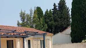 Un área de patio techada con mesa y sillas, sillones de descanso y macetas.