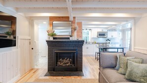 A modern living room with a fireplace, a sofa, and a kitchen in the background.