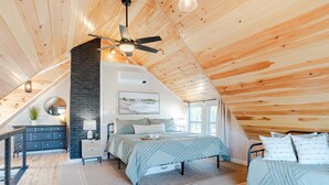 A cozy attic bedroom with a sloped ceiling, a bed, a dresser, and a desk.