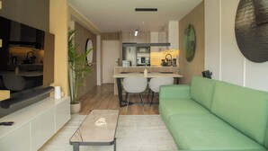 Un salon moderne avec un canapé vert, une table basse et un coin repas, la cuisine étant visible au fond.