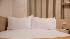 Un lit bien fait, avec du linge de lit blanc et un plaid marron.