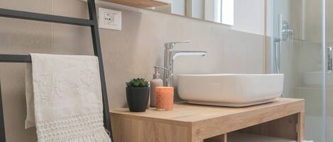 Un baño moderno con tocador de madera, un lavamanos blanco y un perchero para toallas.