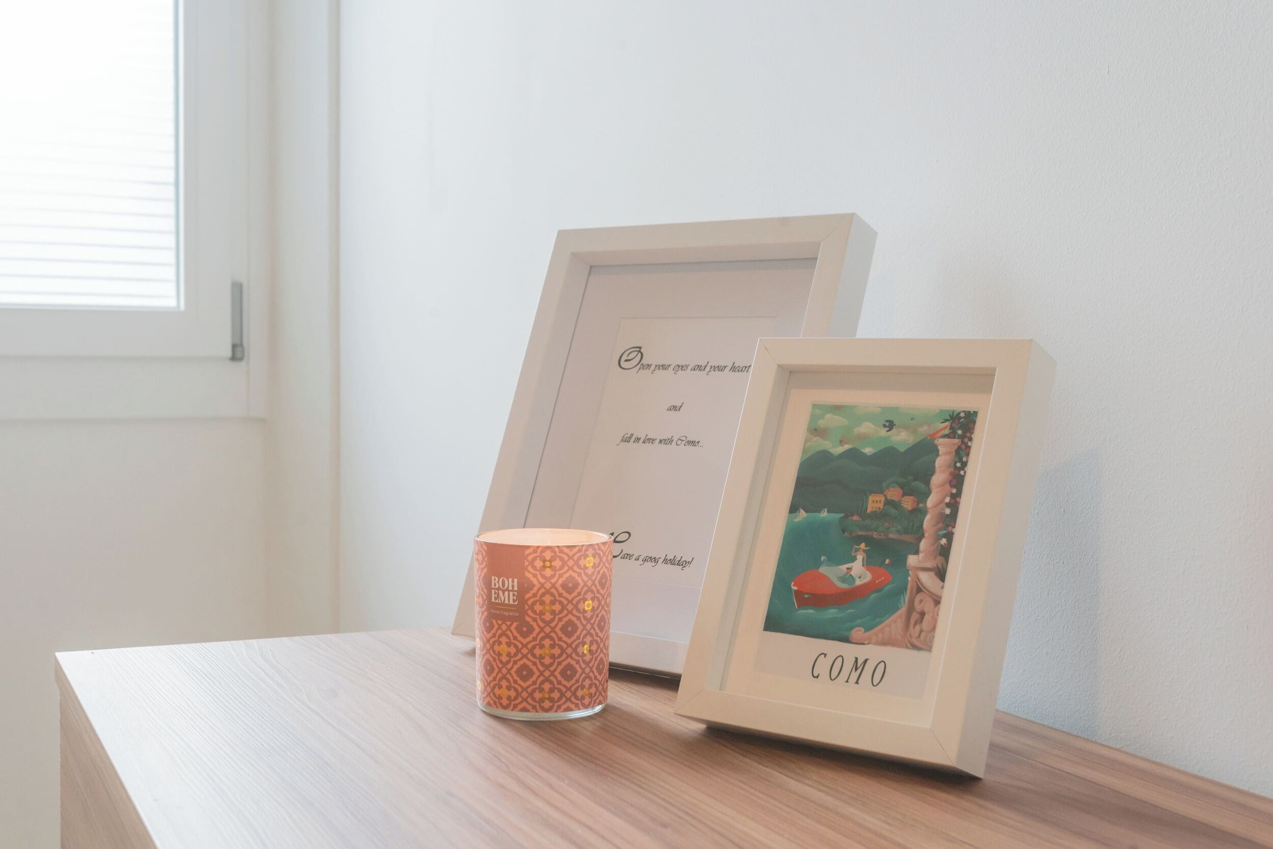 Un quadro incorniciato con la scritta "COMO" e una candela su un piano di legno.