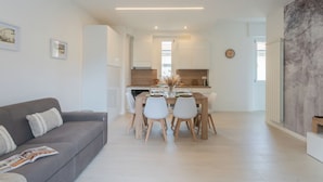 A modern living room with a grey sofa, a dining table set for four, and a kitchen in the background. - Magnolia House Como by Rent all Como (Como)