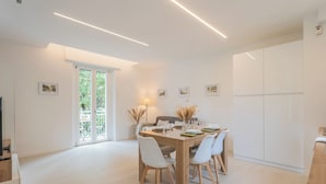 A modern dining area with a wooden table, white chairs, and a glass-top table. There are framed pictures on the walls and a door leading to a balcony. - Magnolia House Como by Rent all Como (Como)