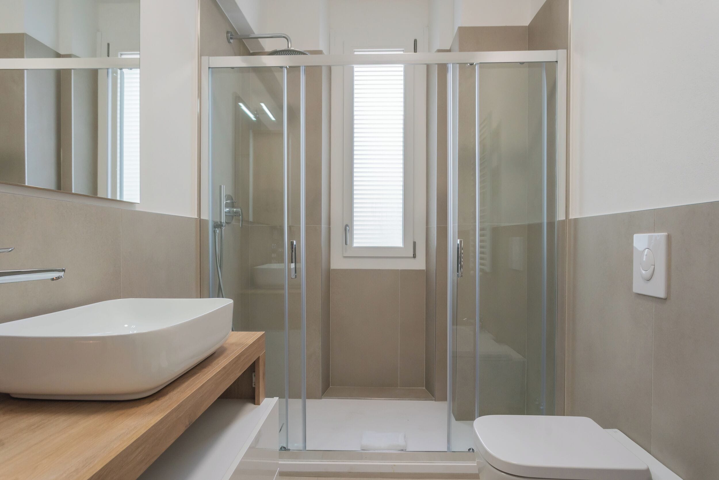A modern bathroom with a large white sink, a glass-enclosed shower, and a toilet.