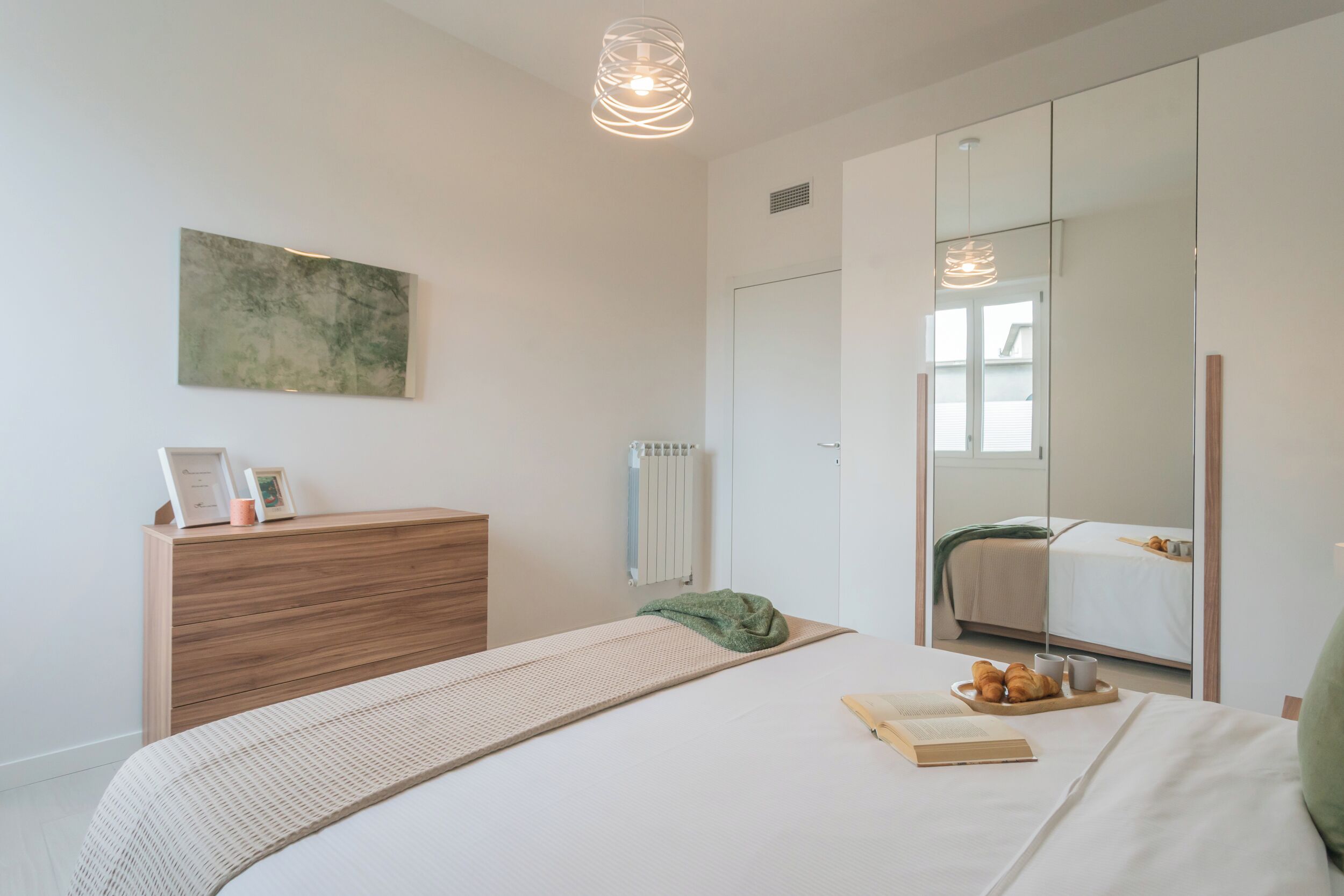 A modern bedroom with a bed, bedside table, and a large mirror.
