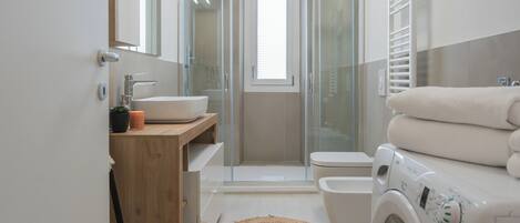 Un bagno moderno con box doccia in vetro, lavandino, WC e lavatrice.