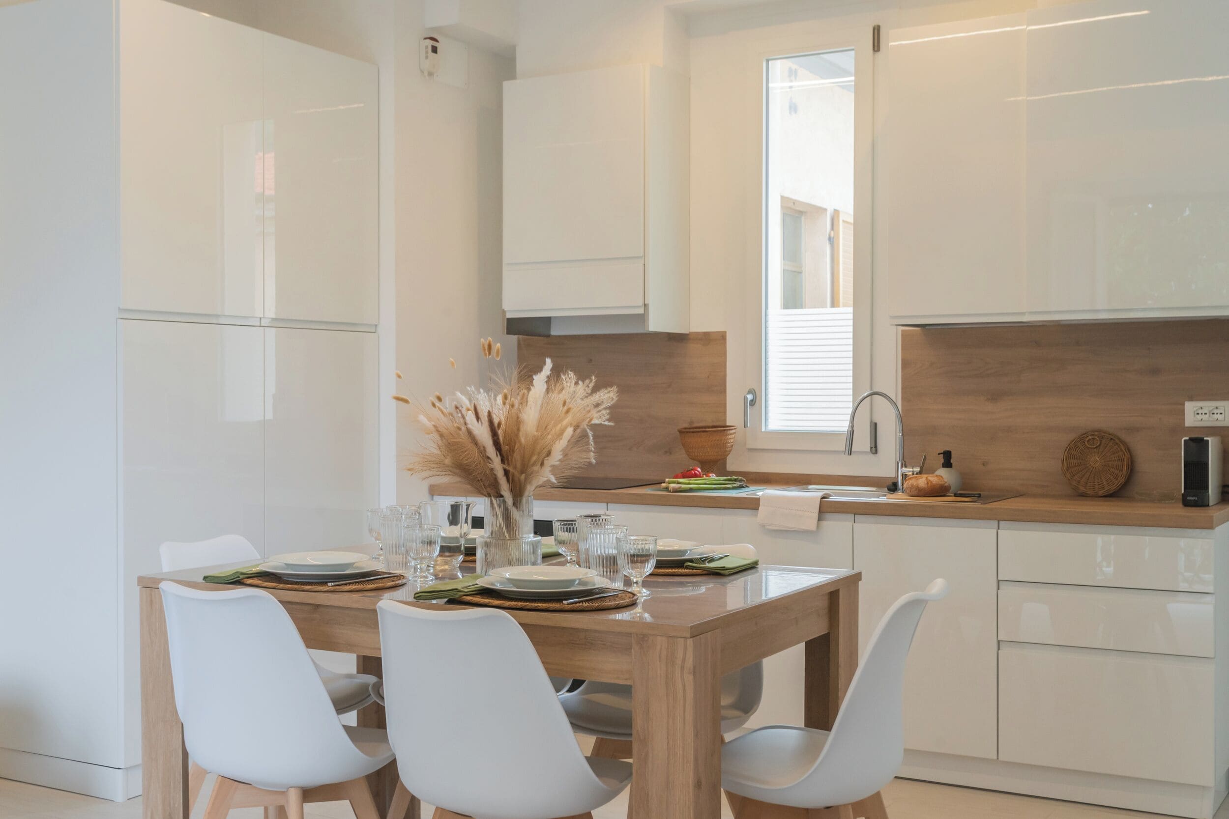 A modern kitchen with white cabinetry, a wooden dining table, and white chairs.