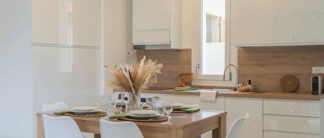 A modern kitchen with white cabinetry, a wooden dining table, and white chairs.