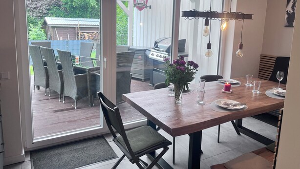 A dining area with a table set for four, a grill outside, and a view of the backyard. - Shed 30 near Hamburg between the seas. Billiards, darts, sauna, very luxurious (Schmalfeld)