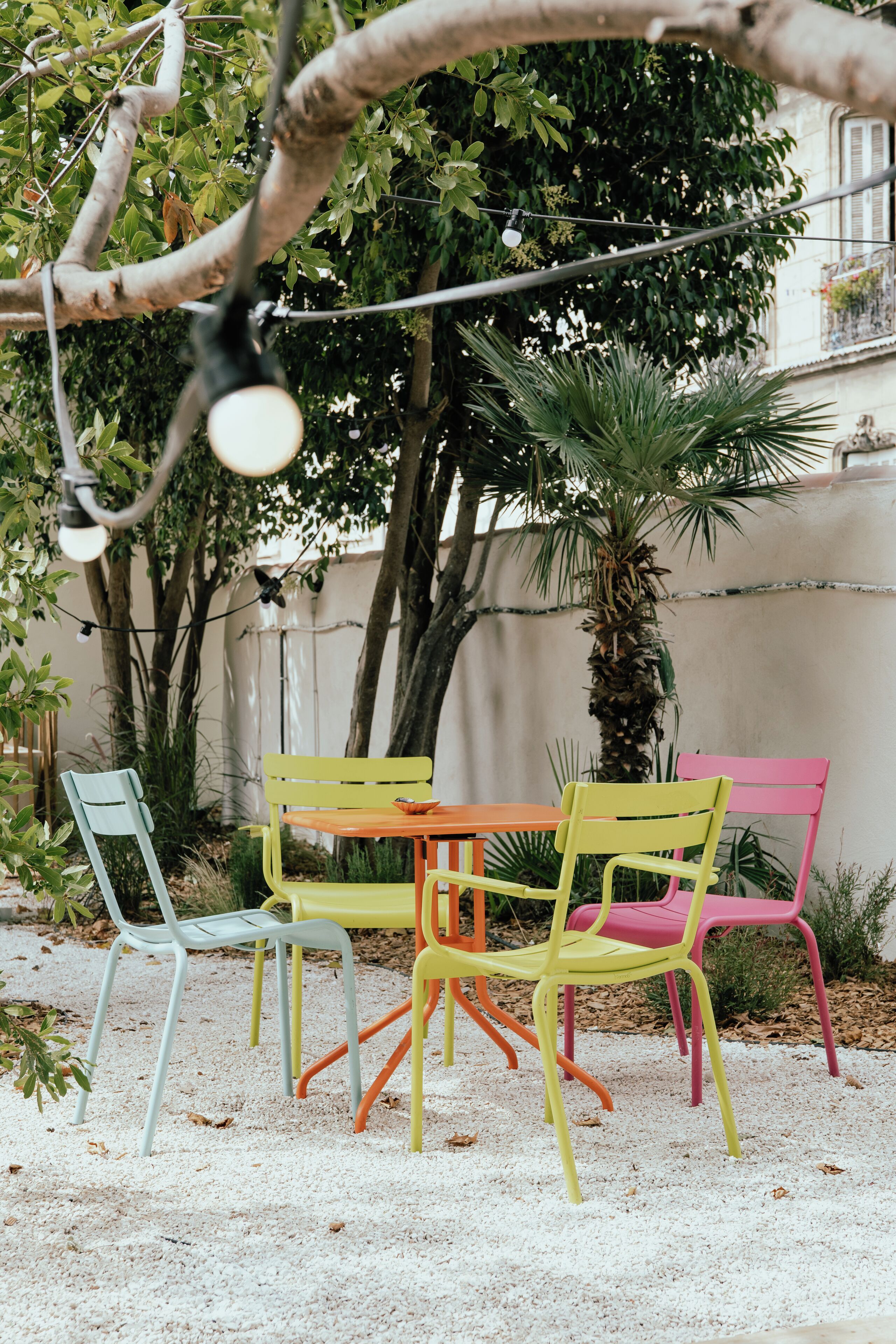 A patio with colorful chairs and a table, surrounded by trees and plants.