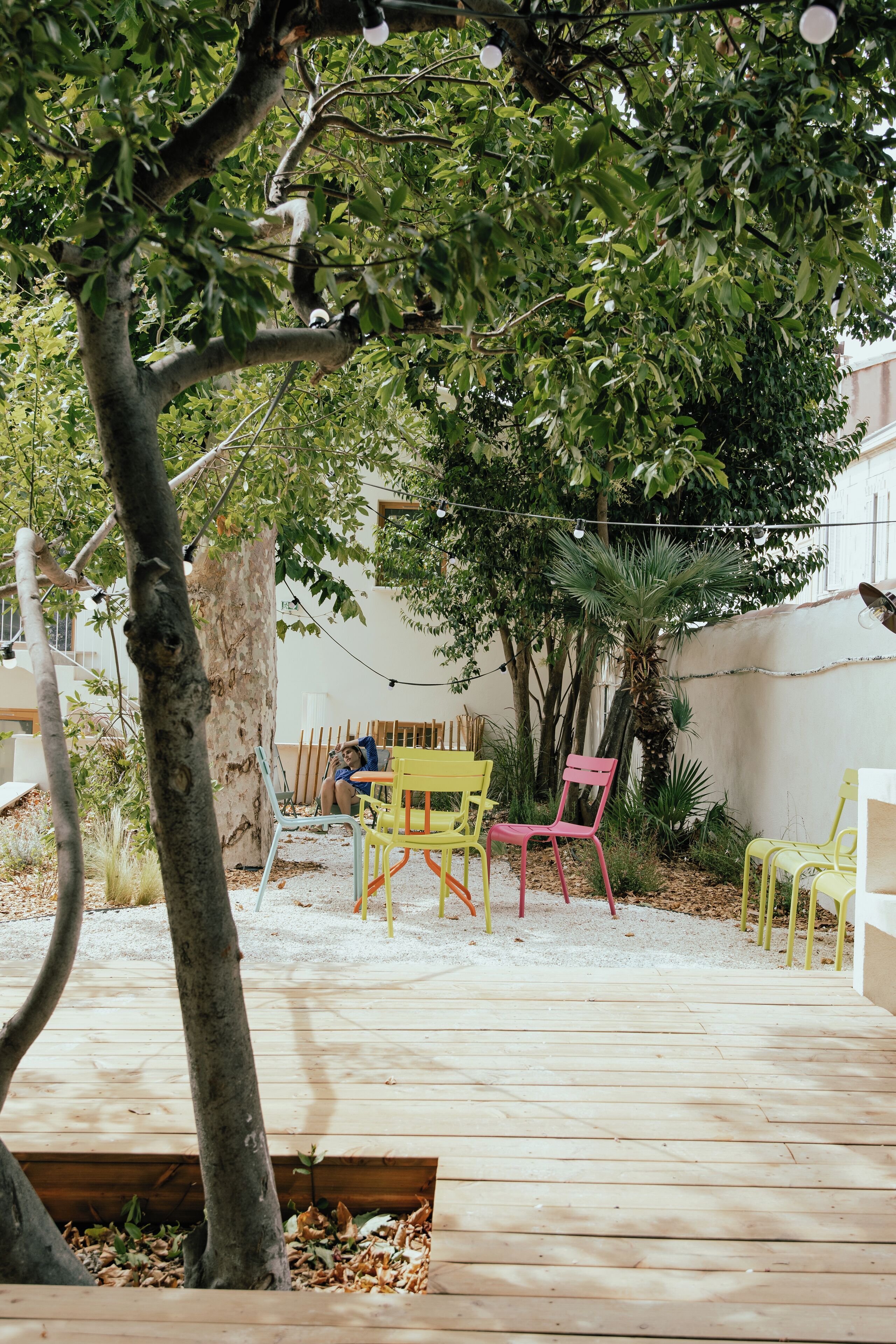 Un patio al aire libre con piso de madera, un árbol y sillas de colores.