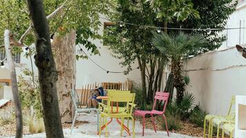 An outdoor patio with wooden flooring, a tree, and colorful chairs.