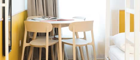 A room with a bed, a table with chairs, and a window with curtains.