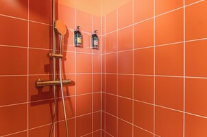 Un baño con azulejos naranja, una ducha con cabezal de ducha manual y dos botellas de champú en la pared.