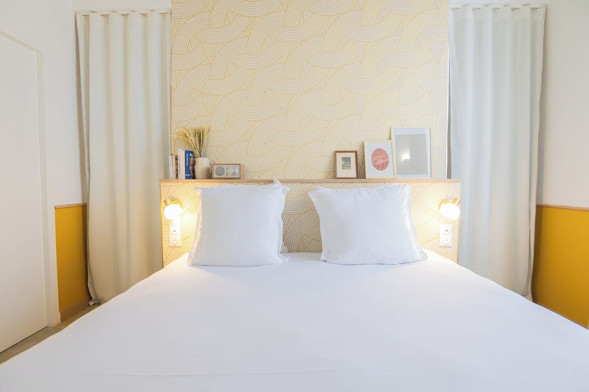 Ein Hotelzimmer mit einem Bett, zwei Nachttischen, einer Wand mit gemustertem Tapetenmuster und einem Fenster mit Vorhängen.