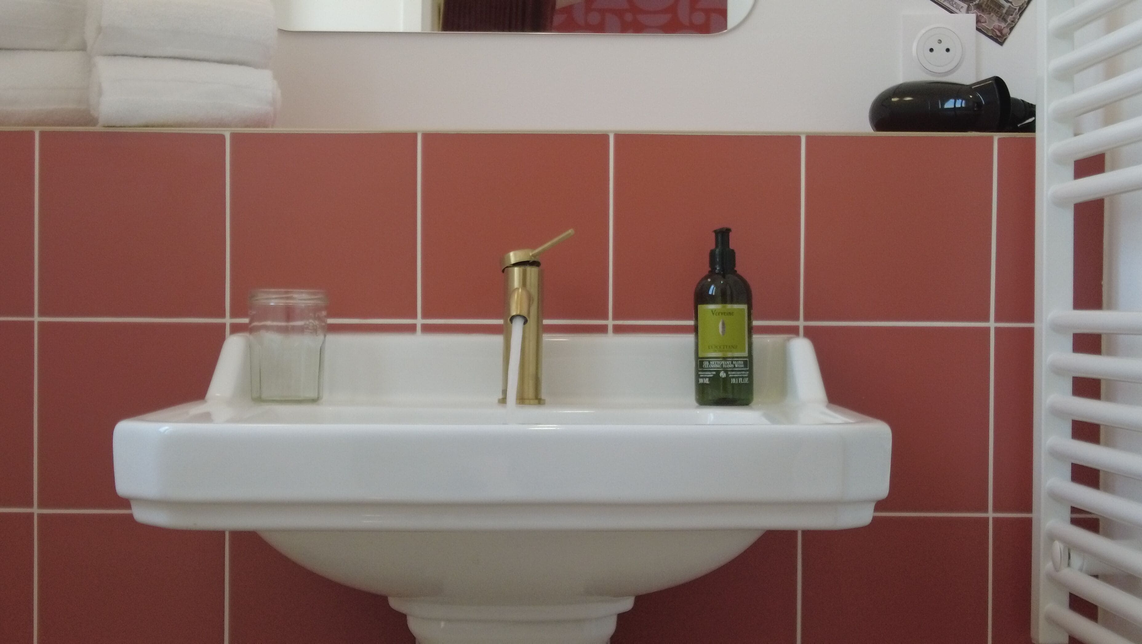 A bathroom sink with a gold faucet, a glass jar, and a bottle of lotion.