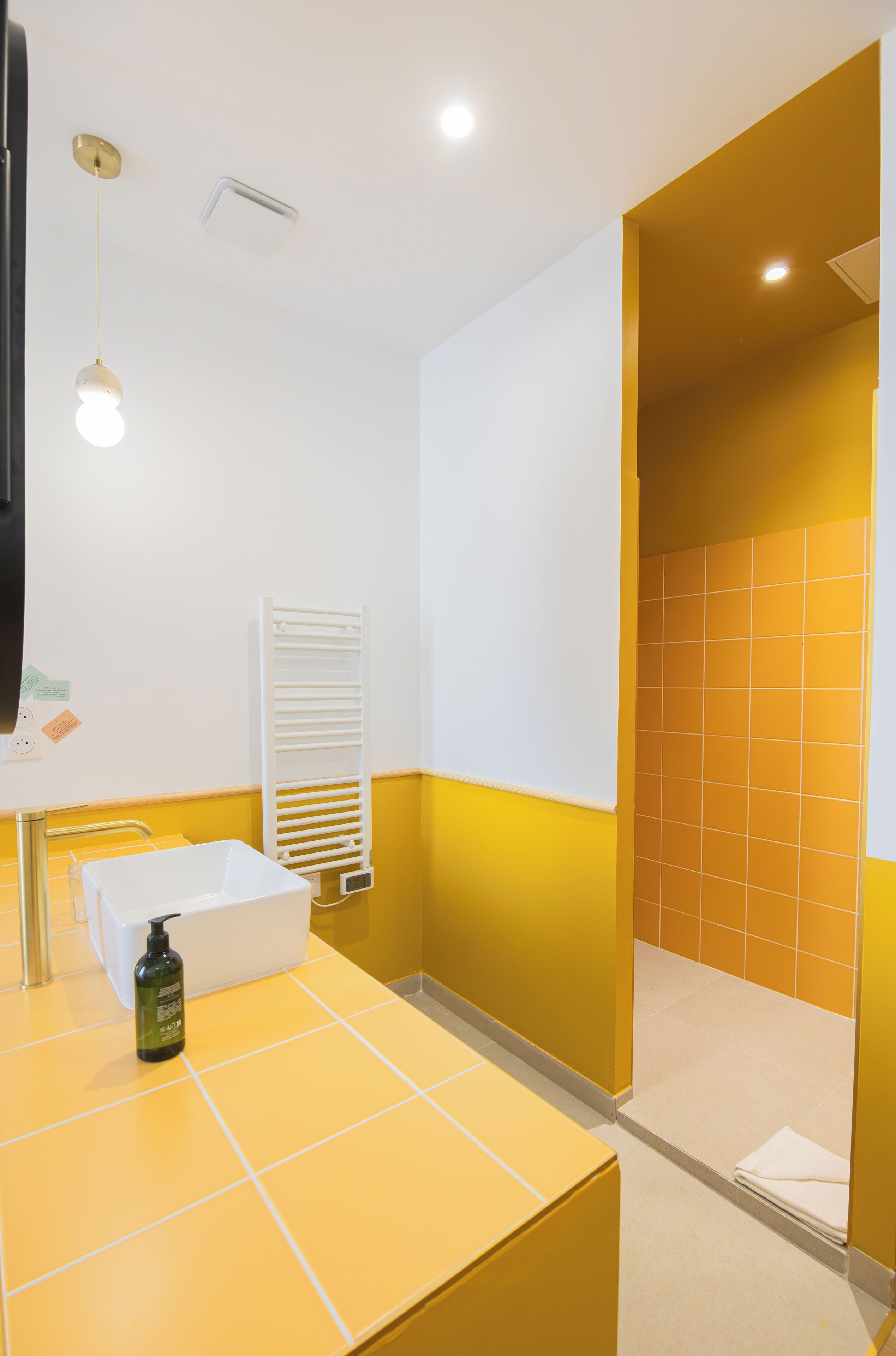 Une salle de bain aux couleurs jaune et blanc, comprenant un lavabo, un porte-serviettes et un espace douche.