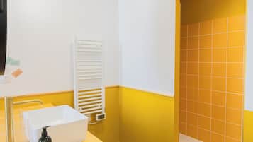 Un baño con una decoración en tonos amarillo y blanco, que incluye un lavamanos, un perchero para toallas y una zona de ducha.