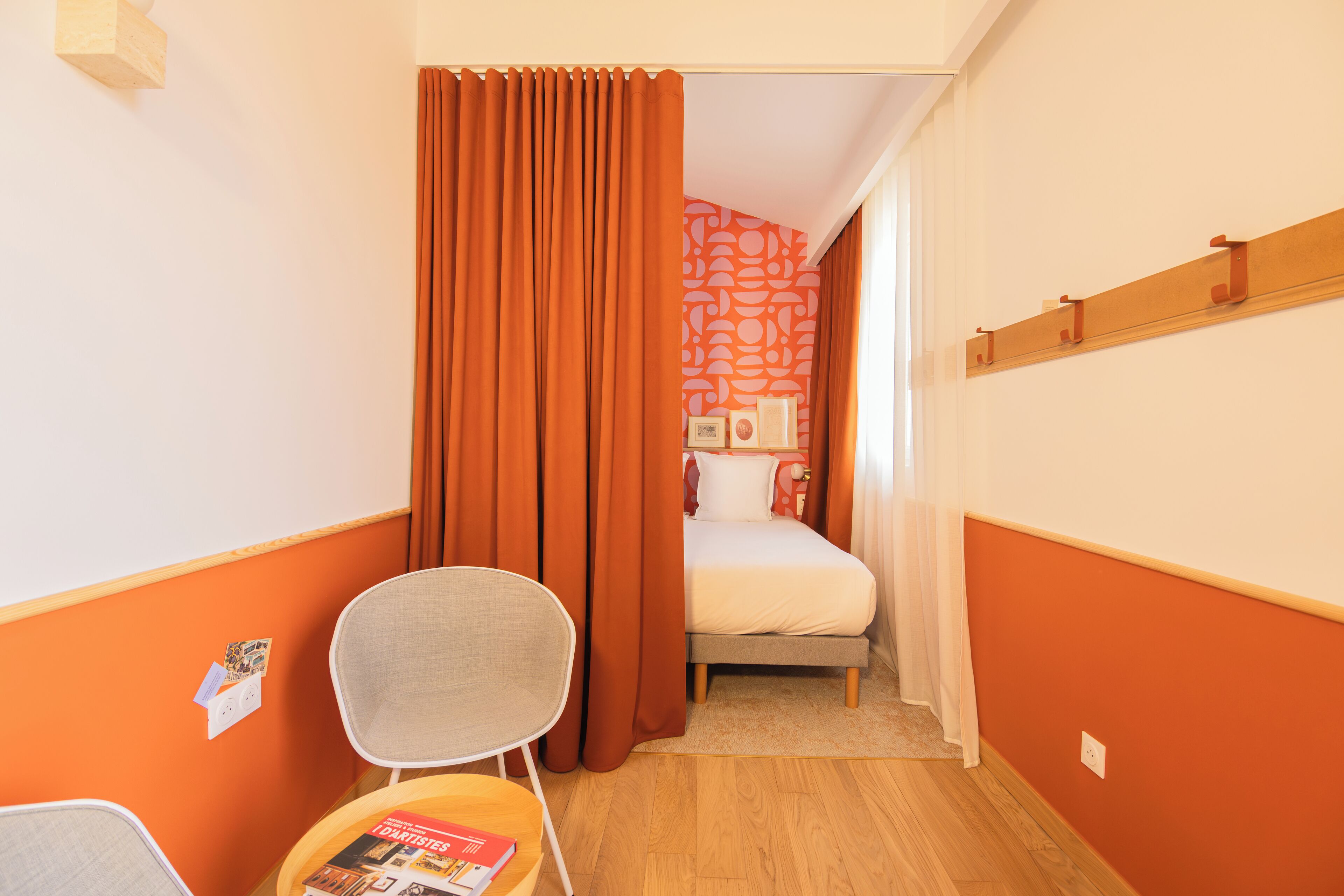 Habitación de hotel con una cama, una silla y una mesita con una revista.