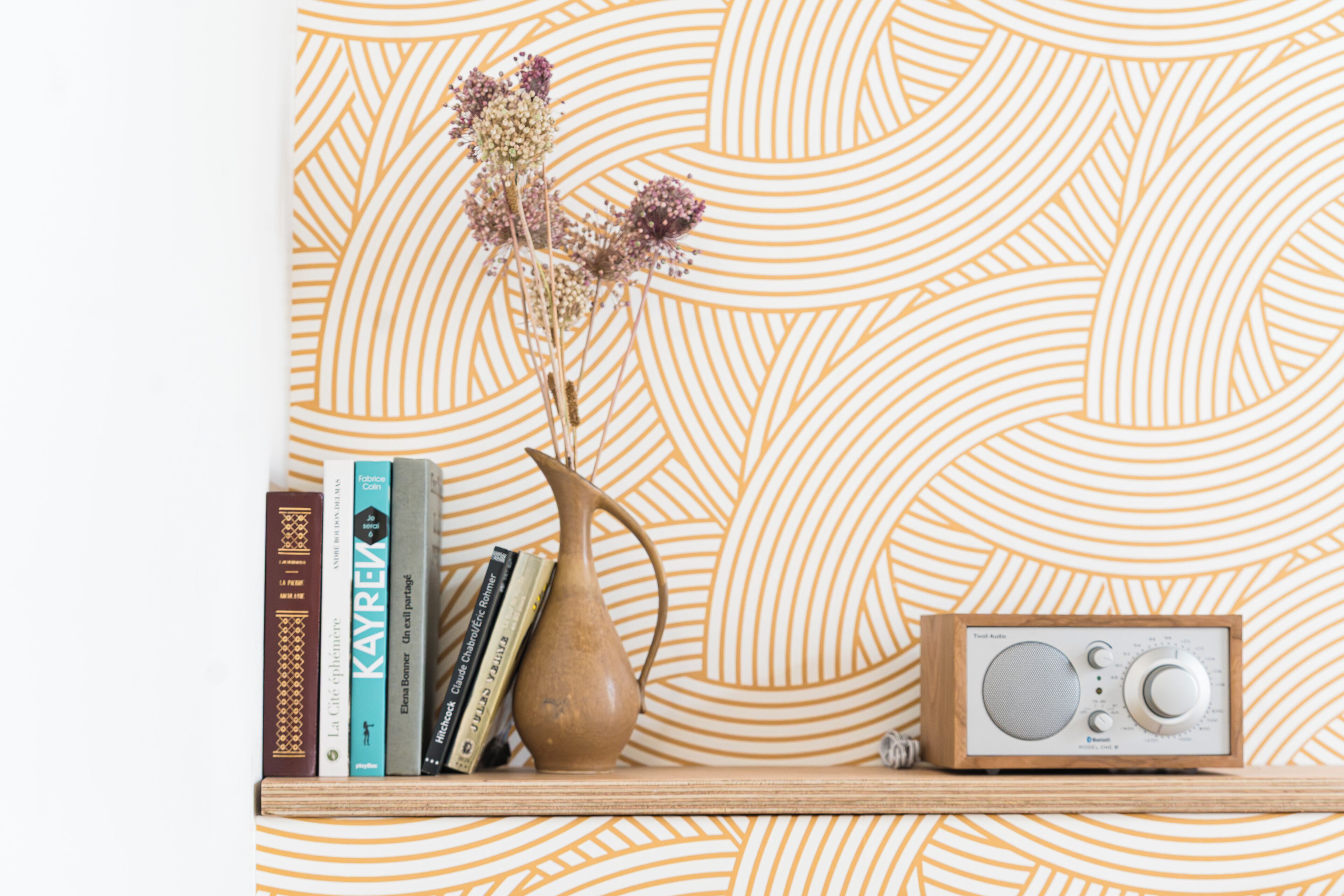 A bookshelf with books, a vase with dried flowers, and a radio.