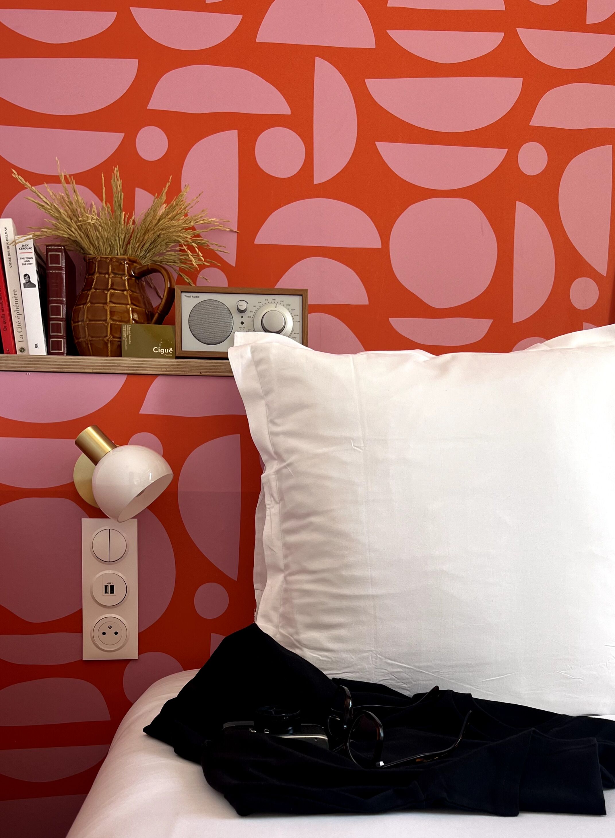 A neatly arranged bedside table with a white pillow, a radio, books, and a vase with dried plants.