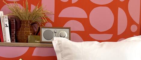 A neatly arranged bedside table with a white pillow, a radio, books, and a vase with dried plants.