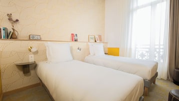 Quarto de hotel com duas camas, uma estante com livros e um rádio, e uma janela com cortinas.