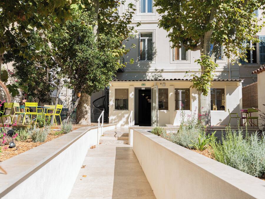 A courtyard with a pathway leading to a building entrance, surrounded by greenery and outdoor seating.